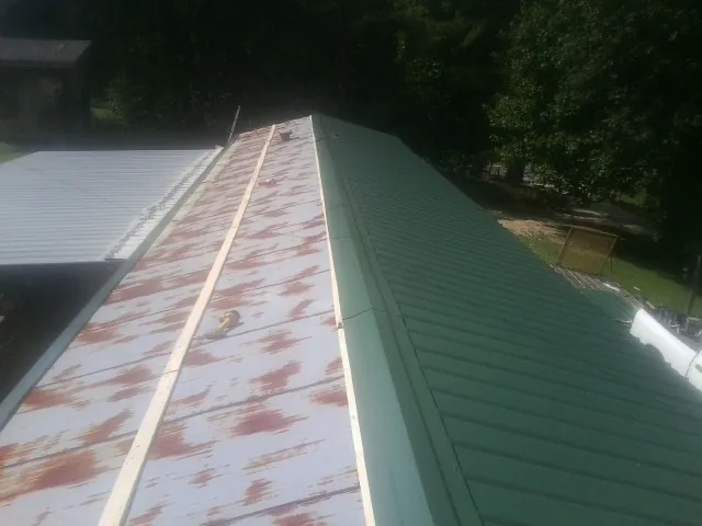 Old rusted panels beside newly installed green metal roofing — Wind Damage Roof Repair by Roofing Brothers in Jasper