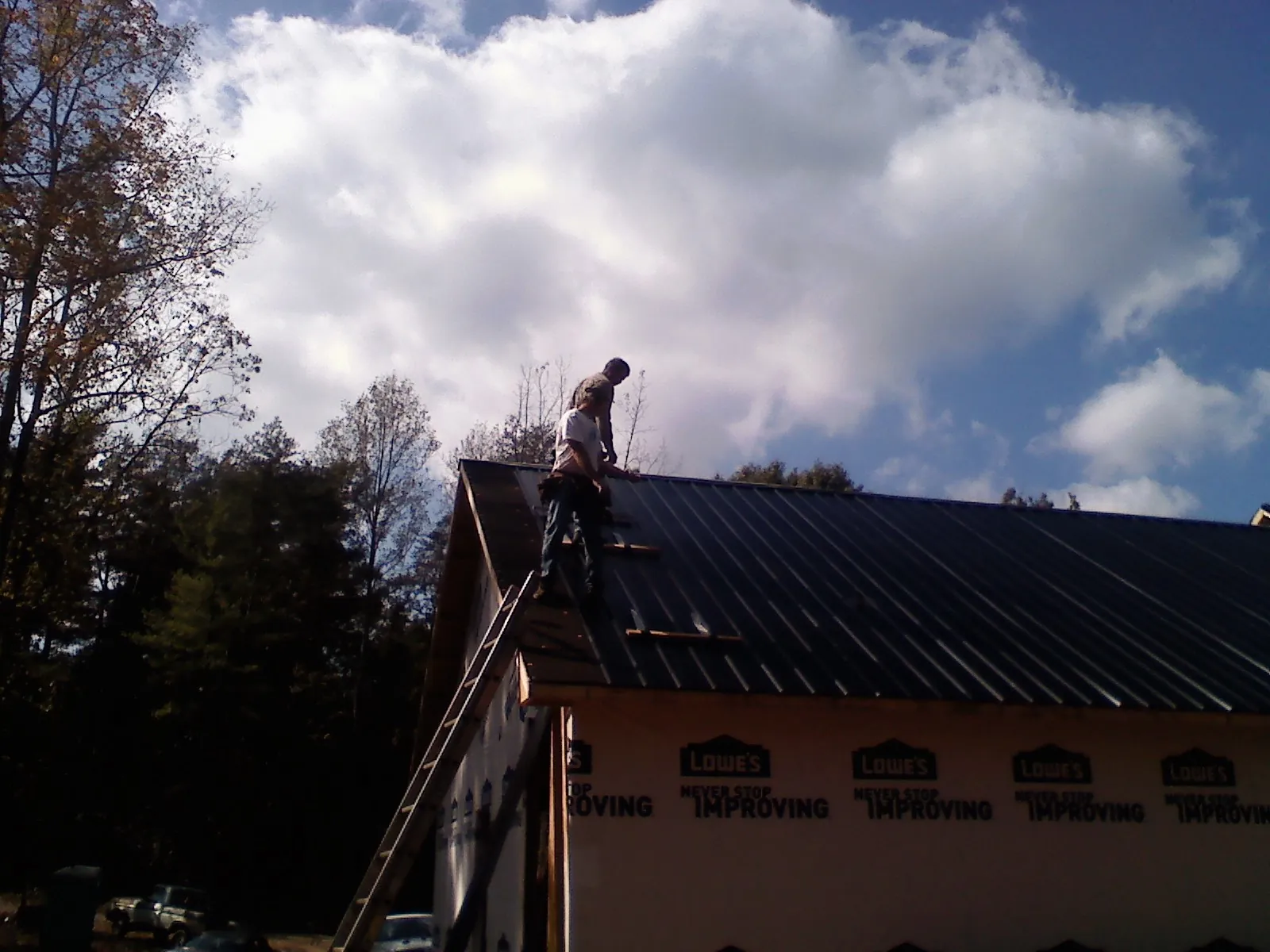 Roofer fastening dark metal panels high against a cloudy sky, from a Roof Inspection job in Jasper